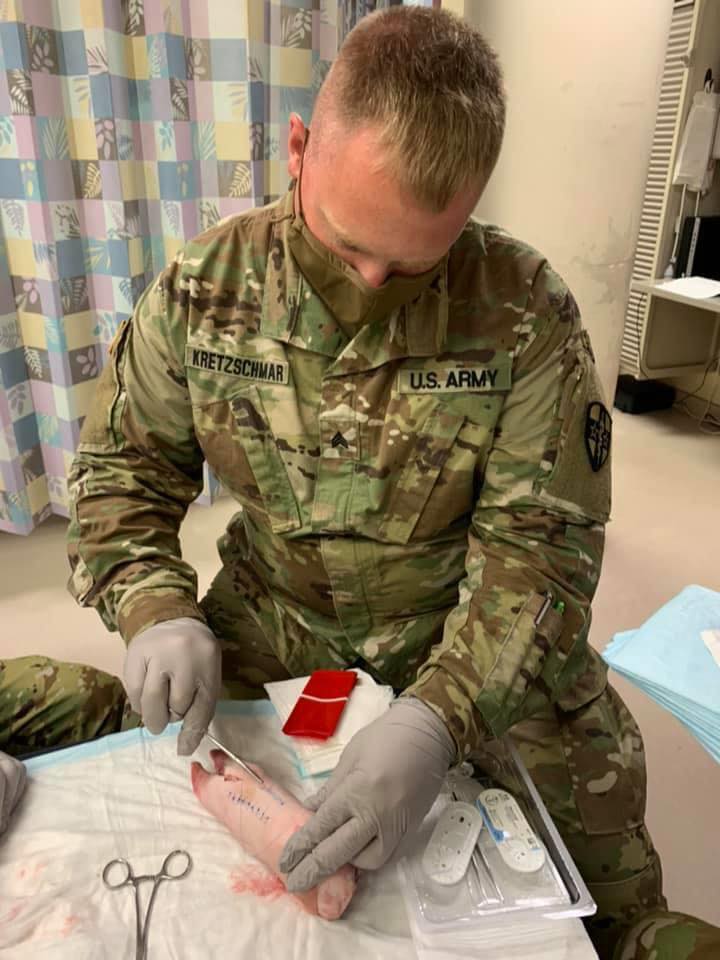 Jordan-Suture-2020 Jordan, a U.S. Army soldier, in uniform and gloves, practices medical procedure on a realistic limb model.